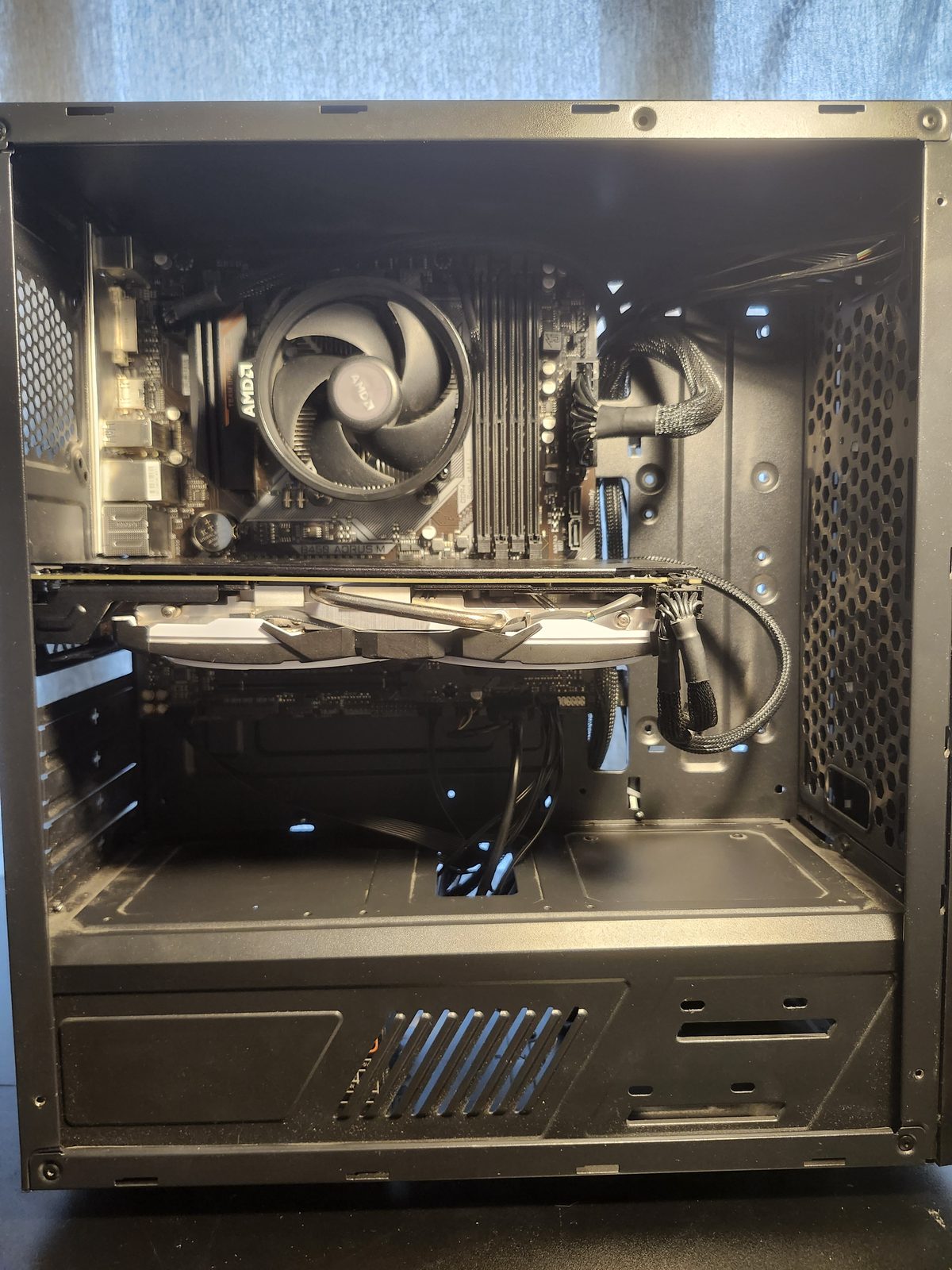 Front interior of a black mid-tower. A stock AMD Wraith cooler sits on the motherboard, the RAM slots are empty, and a white MSI graphics card is installed. Cables are routed along the right side.